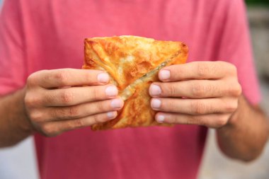 Adamın elinde peynirli börek, atıştırmalık ve fast food konsepti var. Bulanık arkaplan ve metin için kopyalama alanı olan ellere seçici odak.
