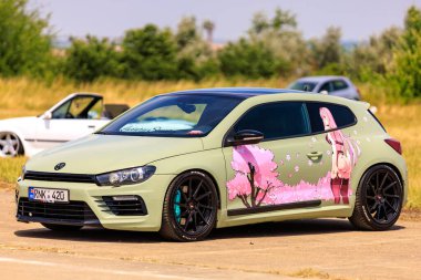 Side view of a customized Volkswagen Scirocco featuring unique anime-themed artwork on the doors, giving it a distinct and creative look. July 2, 2023 Liadoveni Moldova. clipart