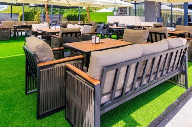 Masaları, sandalyeleri ve büyük bir şemsiyesi olan büyük bir avlu. Masalar beyaz masa örtüleriyle kaplı ve çevrelerinde birkaç sandalye var. Atmosfer davetkar ve rahat. 8 Haziran 2024 Balti Moldova