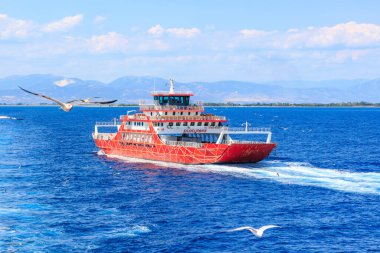 A red boat is sailing on the ocean with a bird flying in the background. The boat is carrying passengers and is heading towards the shore. August 5, 2024 Ferry from Keramoti to Thassos island Greece clipart