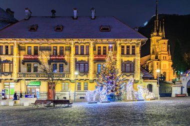 Arka planda bir bina bulunan bir avlunun ortasında bir Noel ağacı var. Avlu ışıklarla aydınlanıyor, neşeli bir atmosfer yaratıyor. 13 Aralık 2024 Brasov Romanya