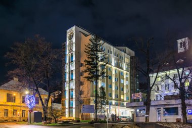 Yan tarafında saat olan büyük bir bina. Bina gece aydınlanıyor. 13 Aralık 2024 Brasov Romanya