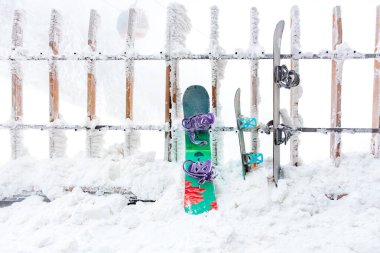 Kar kaplı kayak ve snowboard ekipmanları buzlu ahşap çitte dinleniyor. 15 Aralık 2024 'te Romanya.