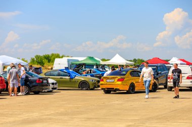 BMW 'nin çeşitli modellerinin olduğu canlı bir sahne, altın sarısı BMW de dahil, araba meraklılarıyla çevrili. 2 Temmuz 2023 Liadoveni Moldova.