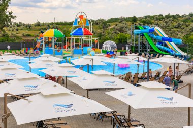 Bir sürü şemsiyesi ve sandalyesi olan büyük bir açık havuz. Şemsiyeler beyaz ve mavidir ve havuz alanına yayılmışlardır. Bölgede birkaç kişi var, bazıları sandalyede oturuyor. 8 Haziran 2024 Balti Moldova