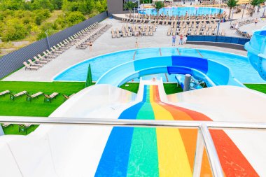Üzerinde gökkuşağı olan renkli bir kaydırak bir su parkında. Kaydırak sandalyeler ve diğer dinlenme odaları ile çevrilidir. 8 Haziran 2024 Balti Moldova