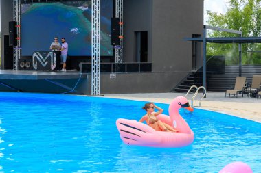 Bir kadın havuzda pembe şişirilebilir bir yüzdürme cihazının üzerinde yüzüyor. Havuz bir sahne ve büyük bir ekranla çevrilidir. 8 Haziran 2024 Balti Moldova
