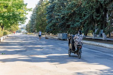 Banliyö sokağında ağaçlar ve bisikletçilerle güneşli bir gün. 9 Eylül 2024 Balti Moldova.