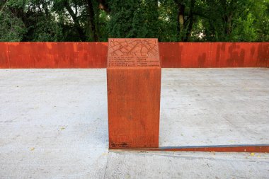 Beyaz tabanlı metal kutu beton bir levhanın üzerinde duruyor. Kutu bir duvarla çevrili ve üzerinde bir plaket var. Plaket yabancı bir dilde ve üzerinde bir harita var. 24 Eylül 2024 Balti Moldova