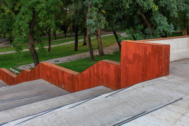 Parka çıkan kırmızı metal adımlardan oluşan bir duvar. Basamaklar betondan yapılmış ve pas renginde. 24 Eylül 2024 Balti Moldova