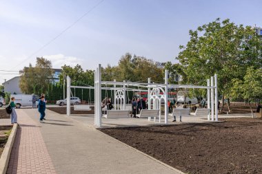Bir grup insan oyun parkının yanındaki kaldırımda yürüyorlar. Oyun alanında banklar ve salıncaklar var. 2 Ekim 2024 Balti Moldova