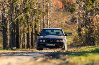 Çıplak ağaçlarla çevrili kırsal bir yolda çekilmiş bir BMW E34 steyşın araba doğal bir ortamda klasik otomotiv tasarımı sergiliyor. Fotoğraf: Leordoaia Moldova, 3 Kasım 2024