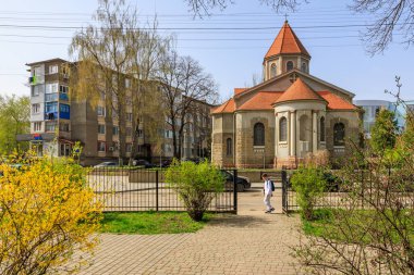 Bir adam kırmızı çatılı bir kilisenin önünden geçiyor. Kilise bir çitle çevrili ve bölgede park edilmiş birkaç araba var. 1 Nisan 2024 Balti Moldova