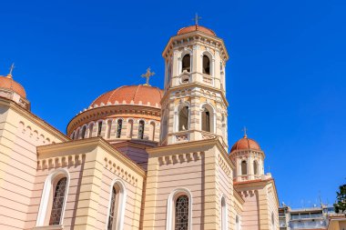 Arka planda mavi gökyüzü olan büyük beyaz ve kırmızı bir bina. Binanın tepesinde büyük bir kubbe ve çan kulesi var.