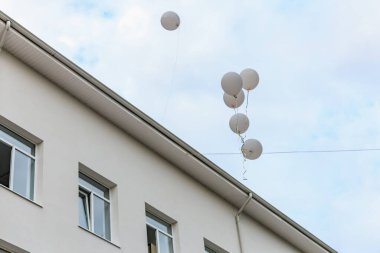 Bulutlu bir gökyüzüne karşı bir binanın üzerinde süzülen beyaz balonlar.