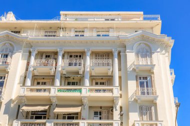 Arka planda mavi gökyüzü ve balkonları olan büyük beyaz bir bina. Binanın klasik ve zarif bir tasarımı var. 8 Ağustos 2024 Selanik Yunanistan