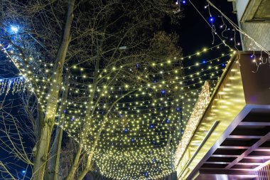 Parlak tatil ışıkları gece açık hava sokaklarını şenlikli bir ışıltıyla süslüyor. 19 Aralık 2024 Balti Moldova.