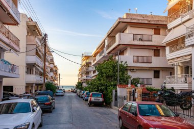 Bir sürü arabası ve birkaç binası olan bir cadde. Sokak ağaçlarla kaplı ve gökyüzü mavi. 8 Ağustos 2024 Perea Yunanistan