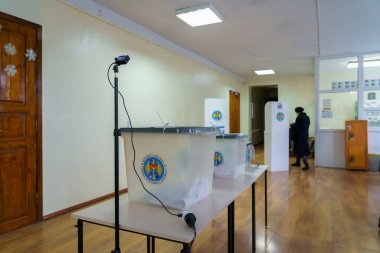 Oy sandıkları olan boş bir oy kullanma merkezi ve yaklaşan bir kadın seçmen. 19 Aralık 2021 Balti, Moldova.