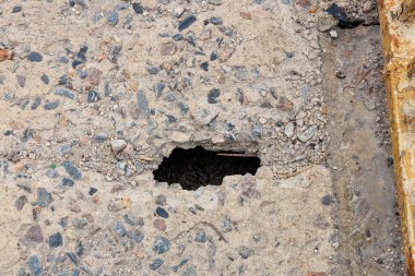 Çürümüş beton yüzeydeki küçük delik altında çakıl dokusunu gösteriyor..