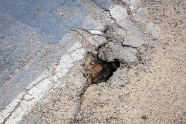 Çatlamış asfalt yolda büyük bir çukur var. Çakıl kenarı yakınlarında..