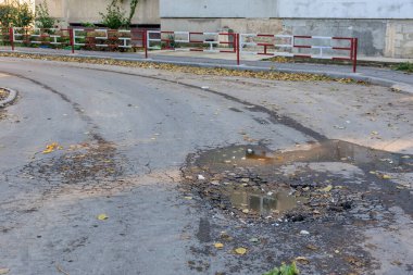 Şehir sokaklarında çukurlar ve su yansımaları olan asfalt bir yol..
