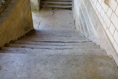 Taş duvarları olan bir bodruma çıkan çatlak beton merdiven..
