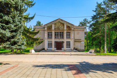 Güneşli bir günde etrafı ağaçlarla çevrili tarihi Sovyet tarzı bir bina. 2 Mayıs 2023 Romanesti Moldova.