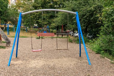 Yeşil şehir parkı ortamında sakin bir günde salıncaklı boş bir oyun alanı. 30 Haziran 2024 Balti Moldova.