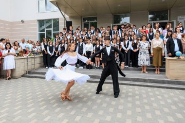 Genç beyaz yetişkinler mezuniyet töreninde öğrenci kalabalığıyla dans ediyor. 2 Eylül 2024 Balti Moldova.