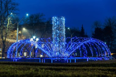 Şehir parkında gece vakti sanatsal ışıklandırmayla aydınlatılmış mavi bir çeşme. 20 Aralık 2024 Balti Moldova.