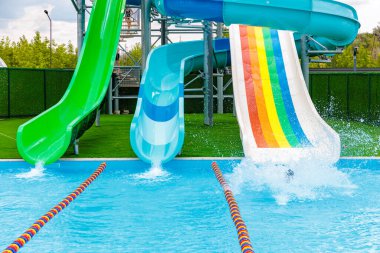 Gökkuşağı kaydırak ve yeşil kaydırak olan bir havuz. Bir kişi havuzda yüzüyor. Sahne eğlenceli ve eğlenceli.