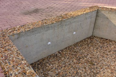 Çakıl tabanlı beton bir duvar. Duvar gri ve üzerinde birkaç delik var. Yapay gölet veya çeşme elementleri.