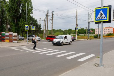 Yaya geçidinden karşıya geçen yetişkin bir kadın, yakınlarda arabalar ve trafik işaretleri var. 26 Temmuz 2023 Beltsy Moldova.