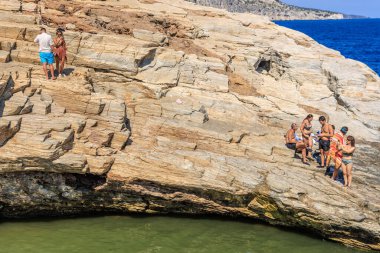 A group of people are sitting on a rock near a body of water. Scene is relaxed and peaceful. August 6, 2024 Giola Thassos Greece. clipart