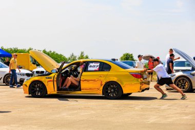 A shiny gold chrome BMW with the hood open, surrounded by people observing and checking details on the vehicle. July 2, 2023. Liadoveni, Moldova. clipart