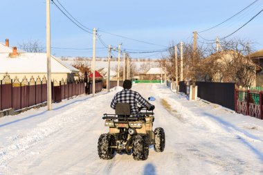 ATV 'li bir adam kışın köyden geçer. Seçici odaklı arkaplan ve metin için alanı kopyala