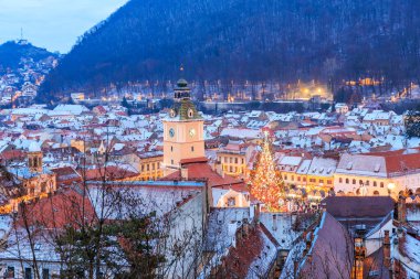Uzun saat kulesi ve merkezinde Noel ağacı olan bir şehir. Şehir geceleri aydınlanıyor, sıcak ve şenlikli bir atmosfer yaratıyor.