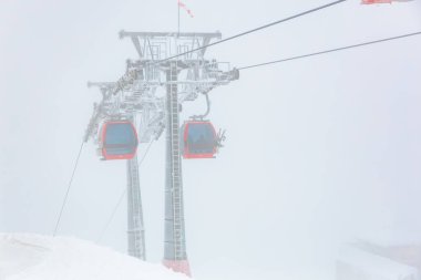 Sisli dağ manzarasında kırmızı teleferikler.