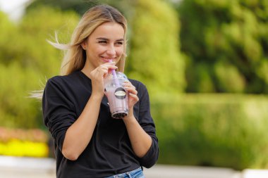 Bir kadın pipetten içki içerken gülümsüyor. İçecek, içinde pipet olan plastik bir bardakta. 15 Eylül 2022 Balti Moldova