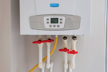 Evde kontrol paneli ve kırmızı valf boruları olan modern gaz kazanı. 29 Eylül 2023 Balti Moldova.