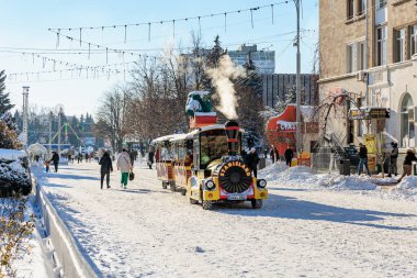 Festive winter street with mini train and snow-covered landscape. January 9, 2024 Balti, Moldova. clipart