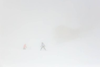 Kayakçılar karlı dağ yamacında bulanık sisli hava koşullarında geziniyorlar.