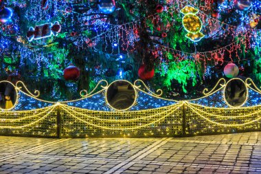 Işıkları ve süslemeleri olan bir Noel ağacı. Işıklar parlak ve renkli, neşeli ve neşeli bir atmosfer yaratıyor.