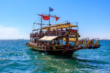 Kırmızı yelkenli ve beyaz tenteli büyük bir tekne okyanusta yüzüyor. Tekne insan kaynıyor ve teknede birkaç bayrak var. 8 Ağustos 2024 Selanik Yunanistan