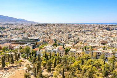 A city view with a lot of buildings and trees. The sky is blue and the sun is shining. August 9, 2024 Athens Greece clipart