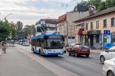 Şehir caddesinde gündüz trafiği ve binaları olan mavi ve beyaz bir troleybüs. 11 Eylül 2024 Balti Moldova.