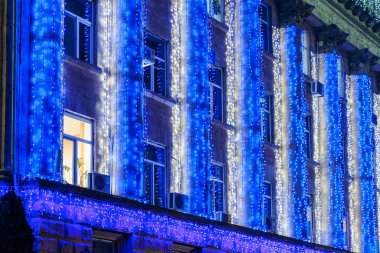 Şehir binasının ön cephesinde şenlikli mavi ve beyaz ışık süslemeleri. 20 Aralık 2024 Balti Moldova.