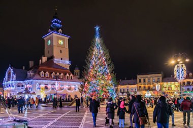 Kasaba meydanında büyük bir Noel ağacı parlıyor. İnsanlar etrafında toplanmış, neşeli atmosferin tadını çıkarıyorlar. 13 Aralık 2024 Brasov Romanya