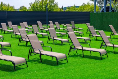 Bir sürü şezlonglu ve çitli büyük bir çimen. Bahçe sandalyeleri boş ve çimenler yeşil.